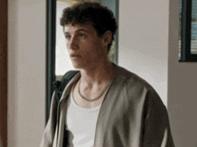a young man with curly hair is wearing a white tank top and a tan jacket .