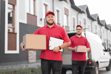 two delivery men in red shirts are carrying boxes and a clipboard