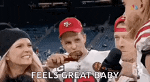 a man in a 49ers hat is eating a piece of meat while a woman holds a child .