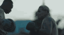 a man wearing boxing gloves is standing next to another man in a dark room .