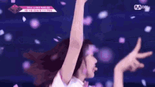 a woman is dancing on a stage with her arms in the air and petals falling around her .