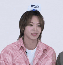 a young man wearing a pink plaid shirt has a sign on his head that says " i am sorry "