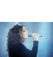 a woman singing into a microphone with her hands up
