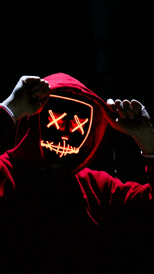 a person in a red hoodie is wearing a neon mask with x 's on it