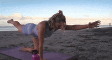 a woman is practicing yoga on the beach with a water bottle