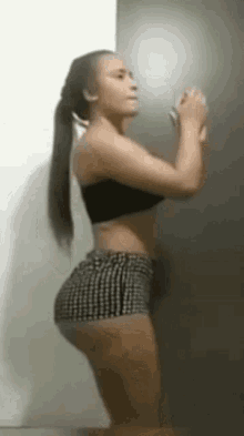 a woman in shorts and a black top is standing in front of a wall .