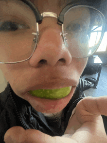 a person wearing glasses is eating a green item