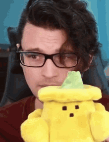 a man wearing glasses is holding a yellow stuffed toy with a green hat on it