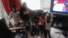 a group of children are standing in a living room and one of them has the number 932 on his shirt