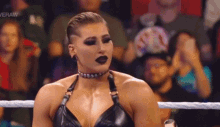 a woman is sitting in a wrestling ring wearing a choker and a black bra .