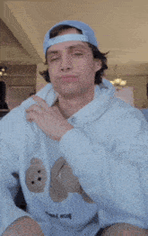a young man wearing a blue hat and a white hoodie is making a funny face
