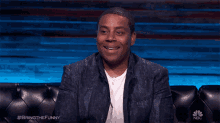 a man is smiling while sitting on a couch with #bringthefunny on the bottom