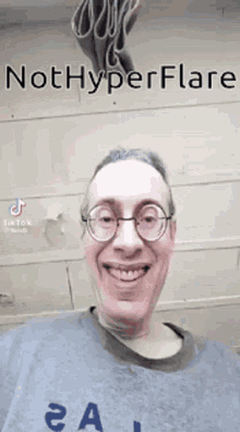 a man wearing glasses and a gray shirt is smiling and looking at the camera .