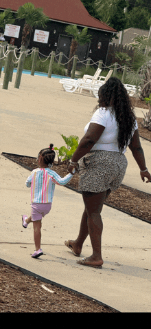 a woman and a little girl are walking down a sidewalk in front of a sign that says " no swimming "