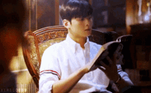 a man in a white shirt is reading a book while sitting in a chair