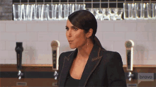 a woman in a black suit stands in front of a bravo sign