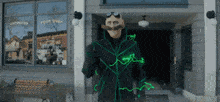 a man with a mustache is standing in front of a building with a green light coming out of his jacket .