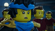 a group of lego figures are standing in a line with one wearing a blue scarf