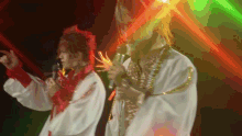 two people singing into microphones on a stage with a green light behind them