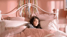 a girl is laying in a bed with pink sheets