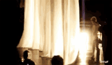 a woman in a white dress is walking on a stage in front of a crowd of people .