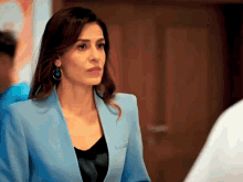 a woman wearing a blue jacket and earrings looks to the side