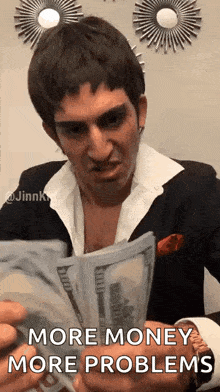 a man in a suit and tie is holding a bunch of money and says `` more money more problems '' .