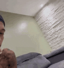 a man with a tattoo on his arm is sitting on a bed in a room with a brick wall .