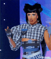 a drag queen is standing on a stage wearing a plaid shirt and denim skirt .