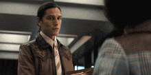 a man in a leather jacket and tie is looking at another man