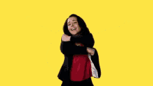 a woman in a red shirt and black jacket with her arms outstretched on a yellow background