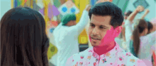 a man with pink paint on his face is looking at a woman in a crowd .
