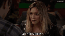 a woman in a leather jacket is talking to a man in a restaurant and asking if he is serious .
