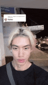 a young man with blonde hair is standing in front of a sign that says ' sybau ' on it
