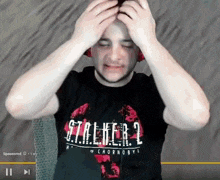 a man wearing a black stalker 2 shirt holds his head