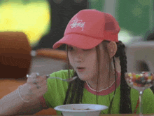 a girl wearing a pink stussy hat is eating from a bowl with a spoon