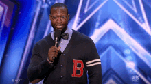 a man wearing a sweater with the letter b on it is speaking into a microphone