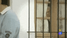 a man in a blue shirt is standing in front of a window with bars and the number 1 on it