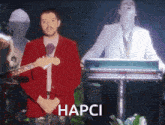a man in a red jacket is playing a guitar and the word hapci is on the bottom right