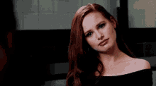 a woman with red hair is wearing a black off the shoulder top and making a funny face .
