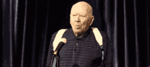 an older bald man is standing in front of a microphone