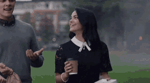 a man and a woman are walking in a park . the woman is holding a cup of coffee .