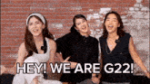 three women are sitting in front of a brick wall with the words " hey we are g22 "