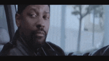a man with a beard is sitting in a car and looking out the window .