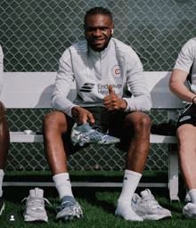a man sitting on a bench holding a pair of soccer cleats and wearing an adidas shirt