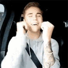 a young man is sitting in the back seat of a car with his eyes closed and his hands in the air .