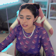 a woman wearing a purple shirt with gengars on it sits in a pink chair