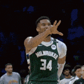 a basketball player wearing a green jersey with the number 34 on it is waving his hand .