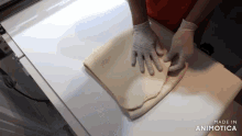 a person wearing gloves is folding a piece of dough and the words made in animotica can be seen in the background