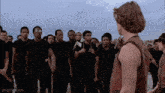 a man in a red tank top is standing in front of a group of men in black shirts .